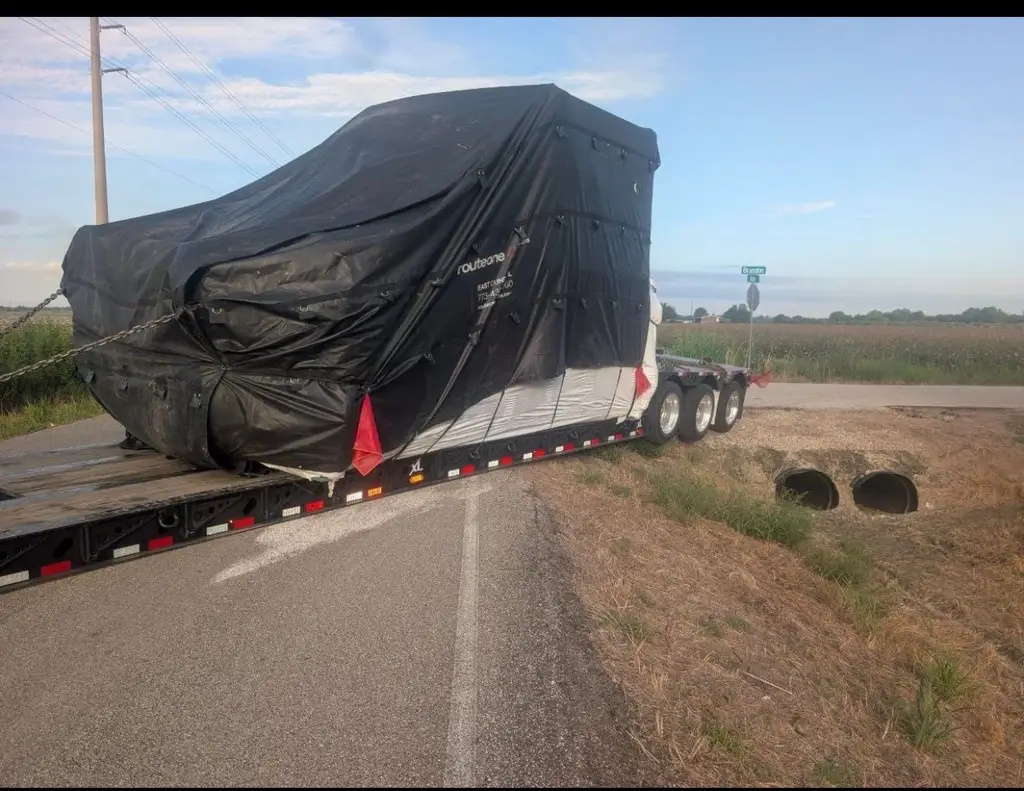 Tarped machinery secured on a low-boy trailer traveling down a highway